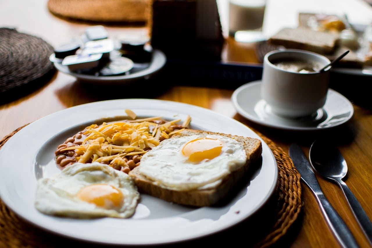 A hearty breakfast with fried eggs, baked beans, and toast served with coffee in a cozy setting.